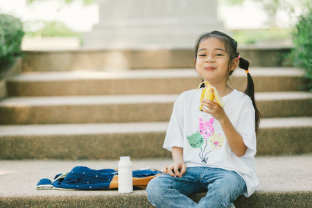Little asian girl sitting on stairs and having breakfast with milk and banana.の写真素材