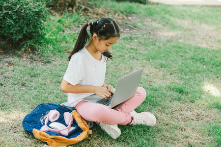 Little girl sitting on grass and using laptop in the park. Education concept.の写真素材