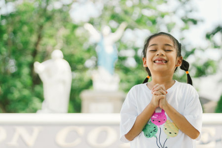 Little asian girl praying in the park with a statue in the backgroundの写真素材