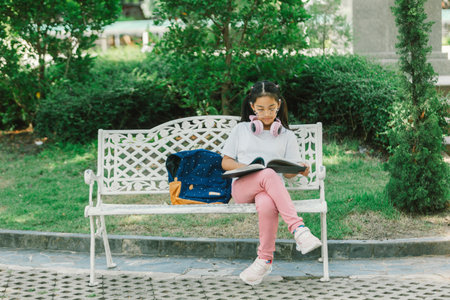 Young asian girl reading a book while sitting on a bench in the parkの写真素材