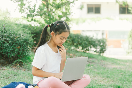 Cute asian child girl using laptop sitting on grass in the park.の写真素材