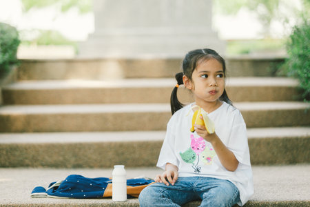 Little asian girl eating banana in the park. Selective focus.の写真素材