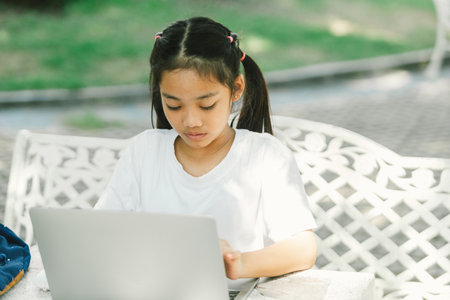 Cute little asian girl using laptop computer while sitting in outdoor cafeの写真素材
