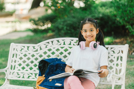 Cute little girl reading a book while sitting on a bench in the parkの写真素材