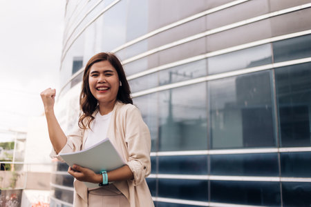 Successful businesswoman standing in front of office building and holding document.の写真素材