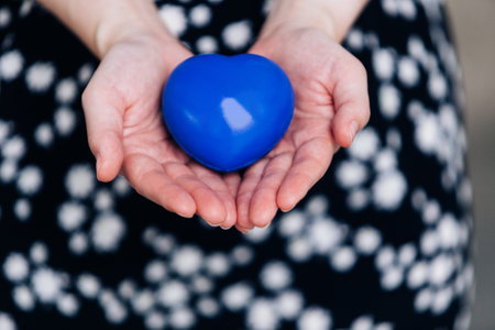 Blue heart in the hands of a woman in a polka dot dressの写真素材