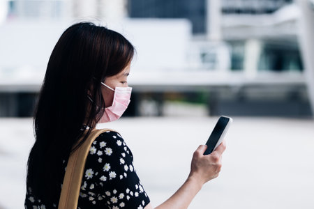 Young woman wearing face mask and using mobile phone in the city.の写真素材