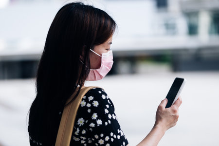 Young woman wearing face mask and using mobile phone in the city.の写真素材