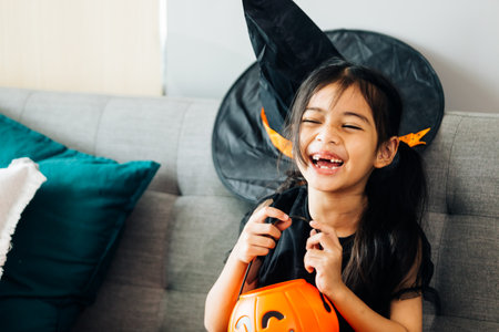 Little girl in halloween costume with jack o lantern on sofaの写真素材