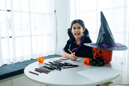 Portrait of little girl in witch costume painting halloween pumpkin on table at homeの写真素材