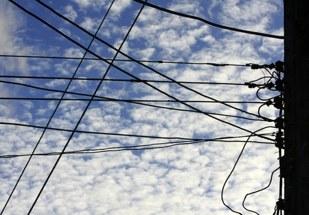 Silhouettes pole and wires against the blue sky with cloudの写真素材