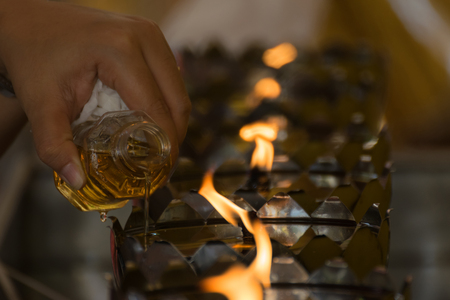 Filling the oil into Thai style metal candle lantern in Thai templeの写真素材