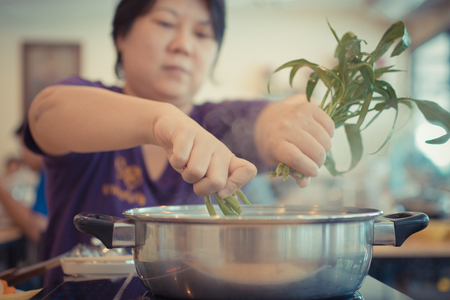 Asia woman plump body cooking food by put a vegetable (morning glory) in to a hot pot for make a...