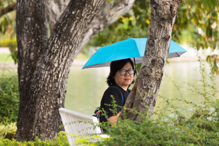 Asia woman plump body with glasses holding a blue umbrella sitting in a parkの写真素材