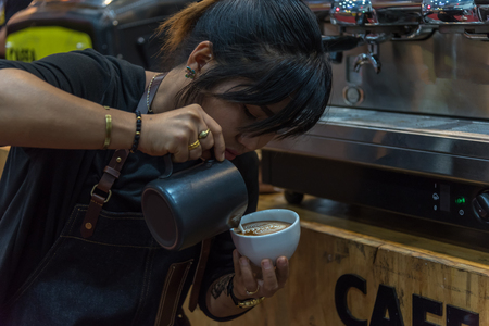 Bangkok, Thailand - March 19, 2017 : Unidentified woman barista pouring latte froth to make a coffee latte art into the white coffee cup for serve to customers in the coffee shop.のeditorial素材
