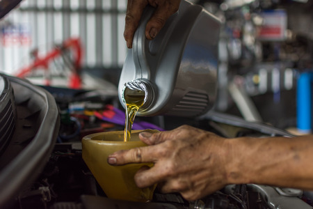 Car mechanic fills a fresh lubricant engine oil at car garage for maintenance a carの写真素材