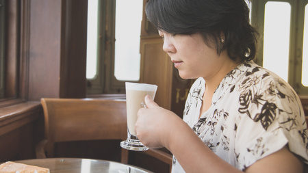 Asian women 40s white skin in white and black dress have a lovely drinking a hot coffee gesture wait for something in a coffee shop cafe vintage styleの写真素材