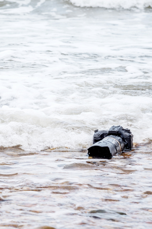 DSLR camera with telephoto lens on a beach it wet from water sea wave when travelの写真素材