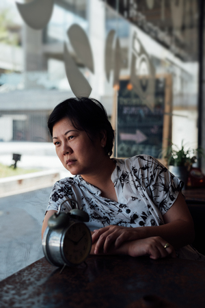 Asian woman 40s white skin plump body in black and white shirt have a bored and unhappy gesture between waiting something in a coffee shop cafe with a clock vintage styleの写真素材