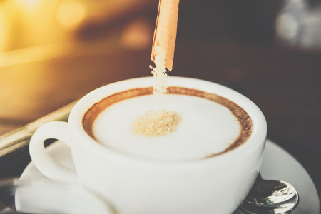 Pouring red sugar in to coffee drink in the white coffee cup on wood table with tea for serve to customers at coffee shop cafe or restaurantの写真素材