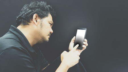Asian man 40s have a short hair in polo shirt strain have a unhappy gesture with failure and problems concept using smartphone on black background dark styleの写真素材