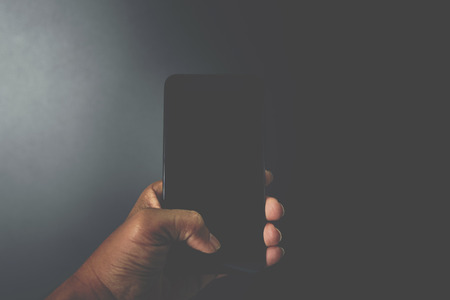 Hand of asian man holding smartphone in technology and communication concept on black background...