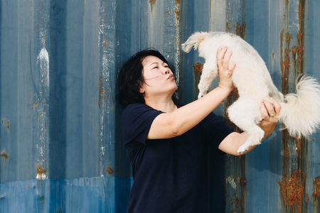 Asian woman and dog happy smile hugging her pat is a dog so cute mixed breed with Shih-Tzu, Pomeranian and Poodle with rusty blue industry container backgroundの写真素材