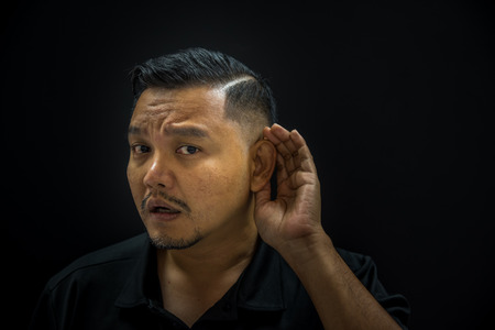 Asian man 40s in black polo shirt have a deaf or hearing with listening silent concept on black background dark styleの写真素材