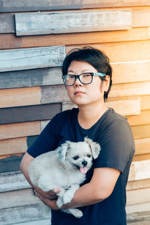 Asian woman and dog happy smile hugging her pat is a dog so cute mixed breed with Shih-Tzu, Pomeranian and Poodle with wooden wall with wood plank background with copy spaceの写真素材