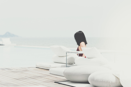 Asian sexy woman in two-piece swimming suit on white beach bed at outdoor swimming pool seaside turquoise sea or ocean with horizon of blue sky at resort or hotel when vacation travel for relaxの写真素材