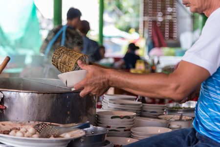 Asian chef cooking a noodle soup with meat ball (kauy-tiew) for sale at Thai street food market or restaurant in Thailandの写真素材