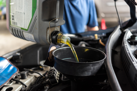 Car mechanic or serviceman fills a fresh lubricant engine oil at car garage for repair or maintenance a carの写真素材