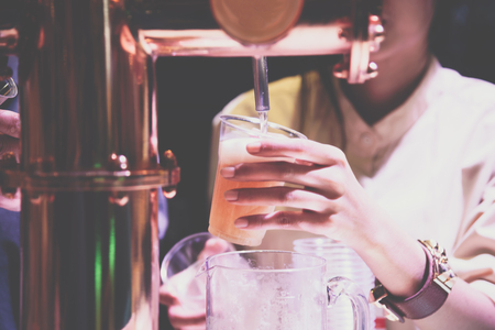 Barman or bartender pouring a drought lager beer from beer tap on counter for serving in a restaurant or pub.の写真素材