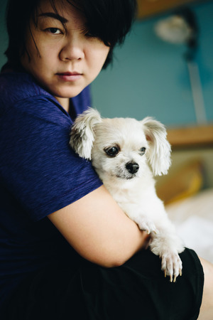 Asian woman and dog happy smile hugging her pat is a dog so cute mixed breed with Shih-Tzu, Pomeranian and Poodle on bed with white veil in bedroom at home or hotelの写真素材