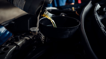 Car mechanic or serviceman fills a fresh lubricant engine oil at car garage for repair or maintenance a carの写真素材