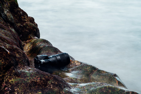 DSLR camera with telephoto lens wet from water sea wave at stone beach when travel and test using in the extreme environment demo waterproof by photographerの写真素材