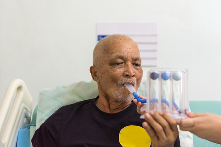 Patient asian elder man 70s use Incentive Spirometer or Triball Tri Flow Meter is medical device to help patients improve the functioning of their lungs on patient bed in ICU. room at hospital.の写真素材