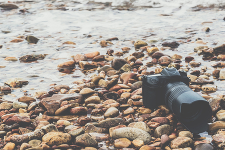 DSLR camera with telephoto lens wet from water sea wave at stone beach when travel and test using in the extreme environment demo waterproof by photographerの写真素材