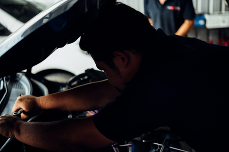 Car mechanic or serviceman checking a car engine for fix and repair problem at car garage or repair shopの写真素材