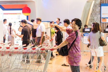 Asian woman feeling happy when her purchase a big product with cartons in shopping cart in department store or exhibit hall expoの写真素材