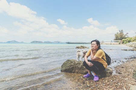 Asian woman and dog so cute mixed breed with Shih-Tzu, Pomeranian and Poodle on rocky beach with happy fun when travel at place with nature beach and tropical sea with blue sky and have rock on beachの写真素材