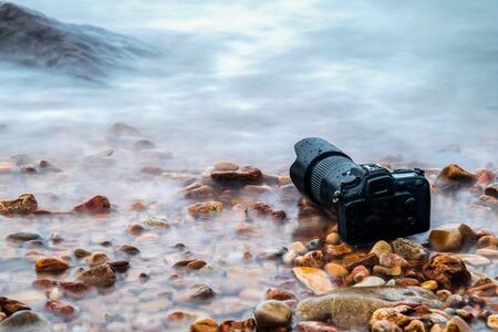 DSLR camera with telephoto lens wet from water sea wave at stone beach when travel and test using in the extreme environment demo waterproof by photographerの写真素材