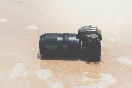 DSLR camera with telephoto lens on a beach it wet from water sea wave when travel and test using in...