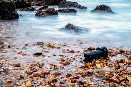 DSLR camera with telephoto lens wet from water sea wave at stone beach when travel and test using in...