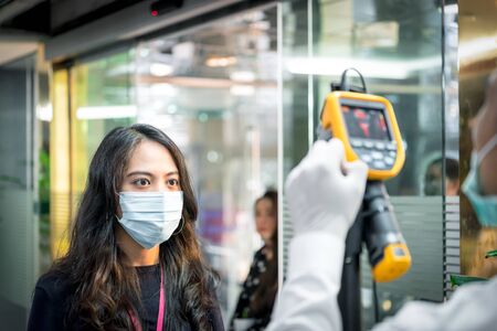 Asian people waiting for body temperature check before access to building for against epidemic flu covid19 or corona virus in office by thermoscan or infrared thermal cameraの写真素材