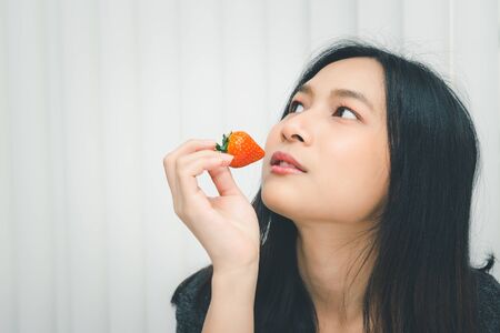 Asian pretty woman holding and eating fresh strawberry is red berry fruit color and sweet juicy with enjoy and happy emotion in concept food, healthy eating in lifeの写真素材