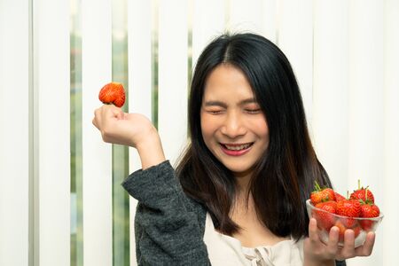 Asian pretty woman holding and eating fresh strawberry is red berry fruit color and sweet juicy with enjoy and happy emotion in concept food, healthy eating in lifeの写真素材