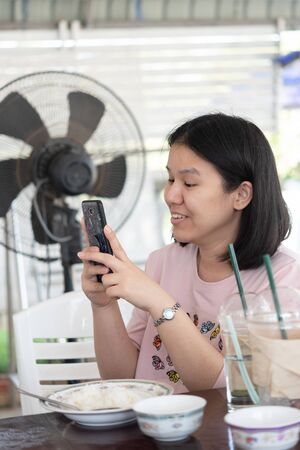 Asian woman foodstagramming use smartphone photographing a food on table in restaurant before eat...