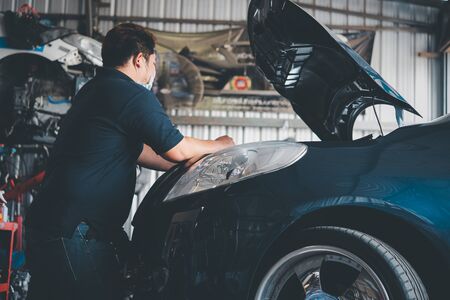 Car mechanic or serviceman checking a car engine for fix and repair problem at car garage or repair...