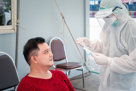 Doctor in PPE suit and asian man patient check by COVID-19 specimen performing a nasopharyngeal or oropharyngeal swab from nasal and oral at hospitalの写真素材